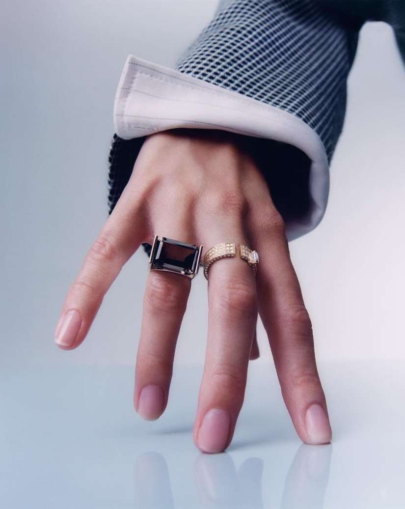Close-up of a person's hand with two rings on fingers, showcasing a large smoky quartz ring and a gold diamond ring, fashion jewelry.