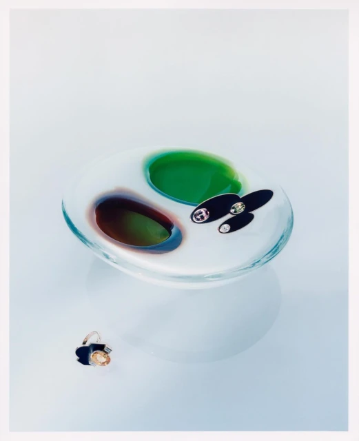 Still life of a clear glass dish with colorful accents and a ring on a white surface, showcasing studio photography of glass art.