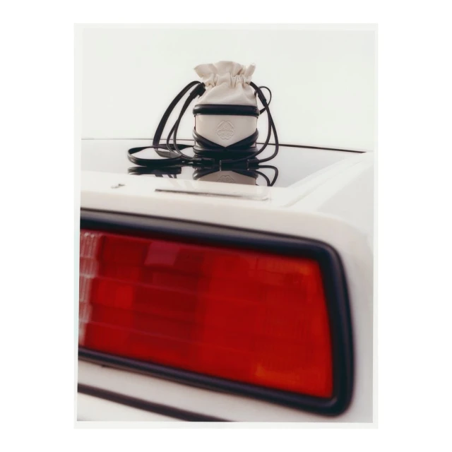 Bucket bag with black straps displayed on the back of a white car, with a red tail light visible in the foreground.