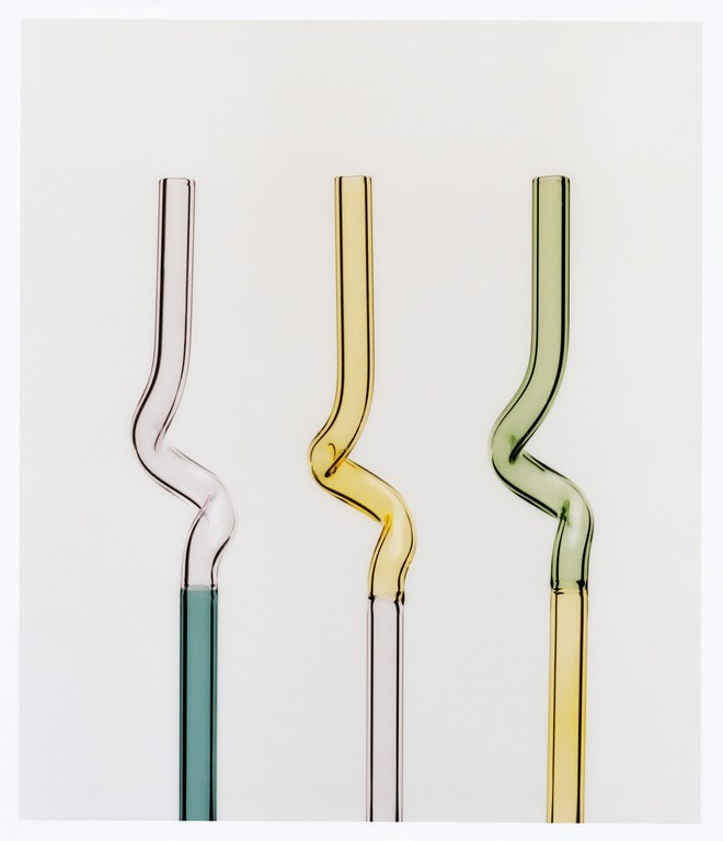 Three colorful, bent glass straws in pink, yellow and green, set against a bright white background in a studio product shot.
