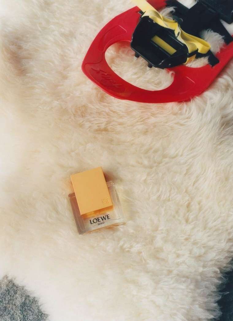 Close-up studio shot of Loewe Solo perfume bottle and red snowshoe against a soft, white, furry background.