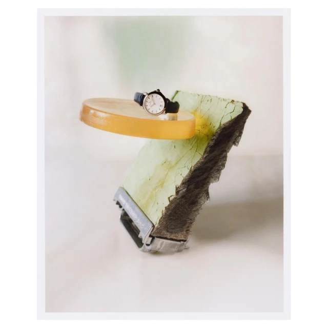 Elegant wristwatch displayed atop a yellow translucent disk and a distressed concrete block against a soft, neutral backdrop.