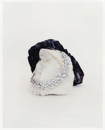 Silver bracelet with geometric pattern resting on a white rock, with a black rock behind against a plain white background. Minimalist jewelry.