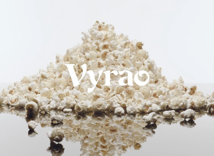 Close-up studio shot of a pile of popcorn on a reflective surface against a white backdrop with the word “Vyrao” displayed in white font.