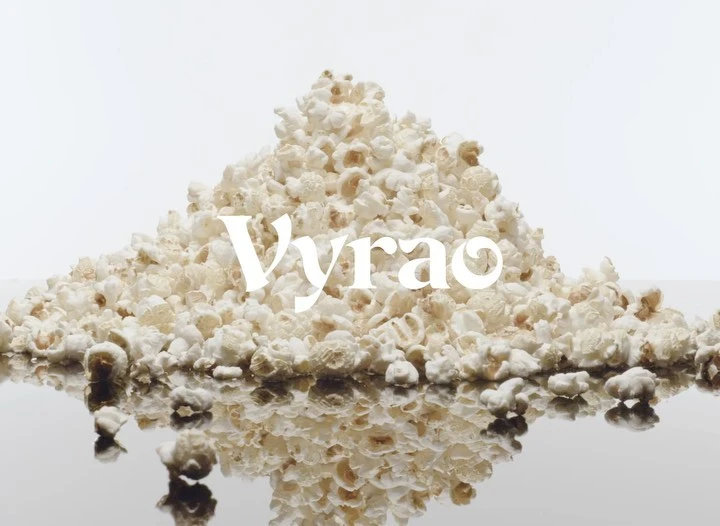 Close-up studio shot of a pile of popcorn on a reflective surface against a white backdrop with the word “Vyrao” displayed in white font.