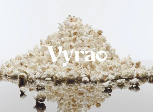 Close-up studio shot of a pile of popcorn on a reflective surface against a white backdrop with the word “Vyrao” displayed in white font.