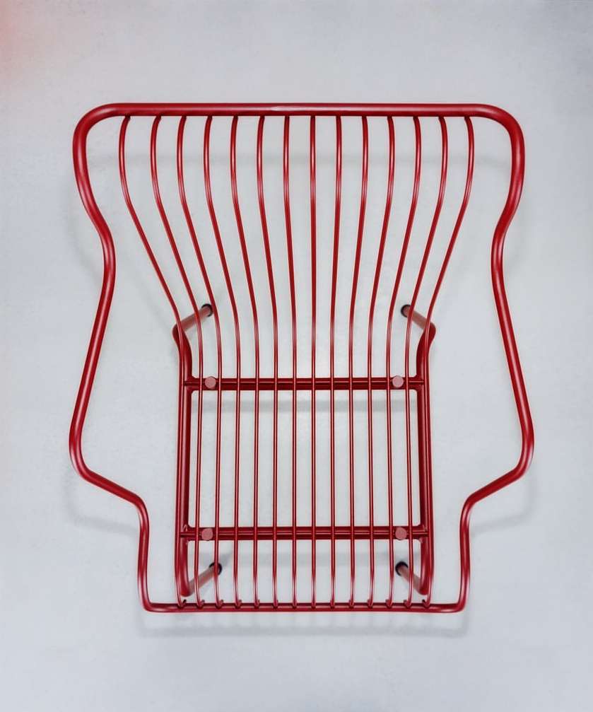 Elevated view of a red painted wire chair featuring an open, linear design on a light grey studio background, creating a minimalist aesthetic.