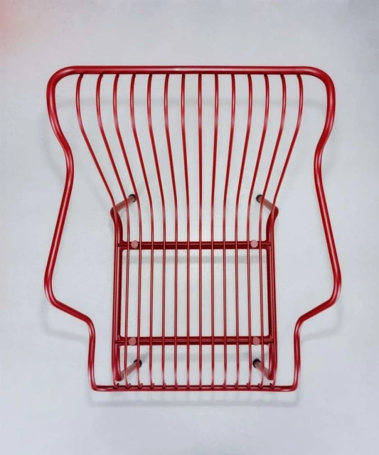 Elevated view of a red painted wire chair featuring an open, linear design on a light grey studio background, creating a minimalist aesthetic.