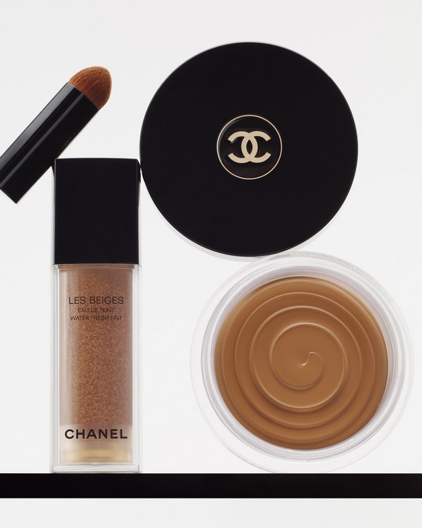 Chanel makeup products including foundation, bronzer, and a blending brush on a white surface. High-angle product shot.