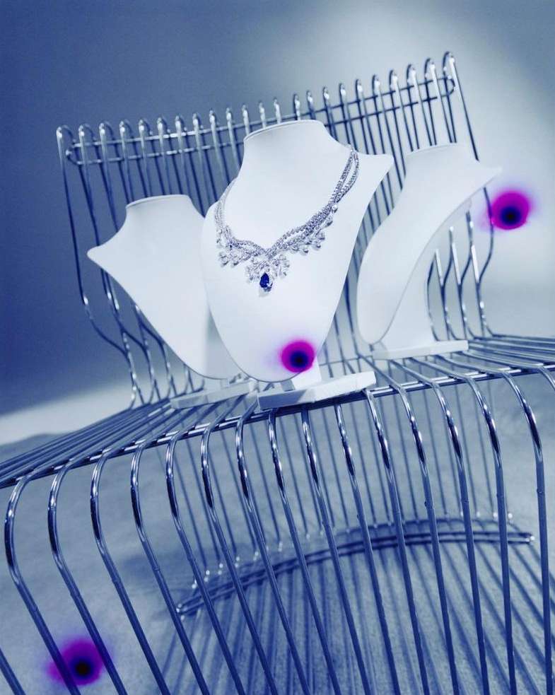 Elegant diamond and sapphire necklace showcased on a white bust against a cool-toned, modern wire rack background.