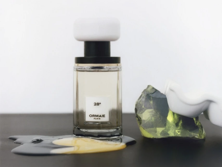 A bottle of Ormaie Paris perfume with a white cap and green stone on a black surface against a bright background.