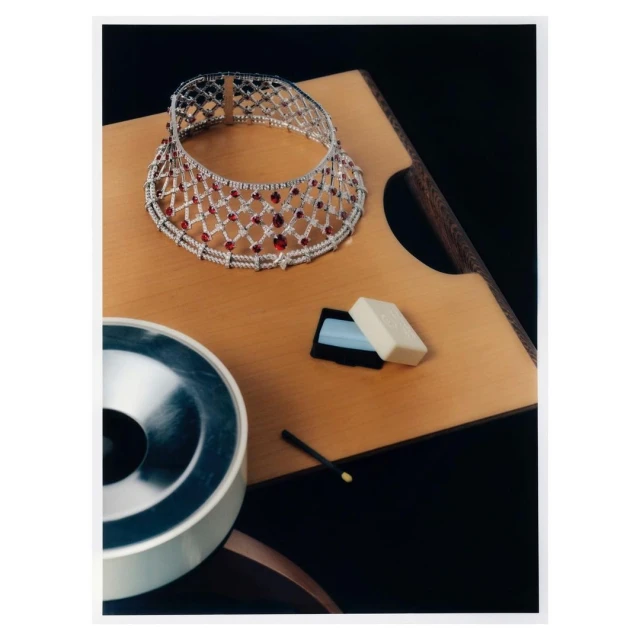 Elegant silver and red gem choker necklace displayed on a wooden surface with styling objects and a dark background, fashion jewelry.