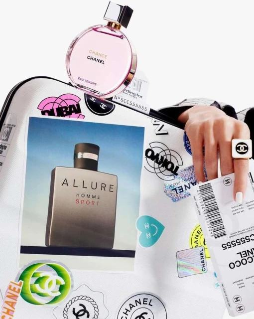 Chanel Chance Eau Tendre and Allure Homme Sport fragrances on a white suitcase with decorative stickers and a hand wearing a logo ring.