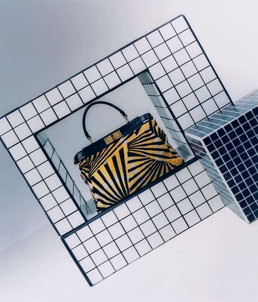 Fashion handbag with a yellow and black radial pattern design, presented in a contemporary display with geometric structures.
