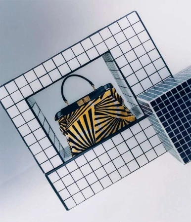 Fashion handbag with a yellow and black radial pattern design, presented in a contemporary display with geometric structures.