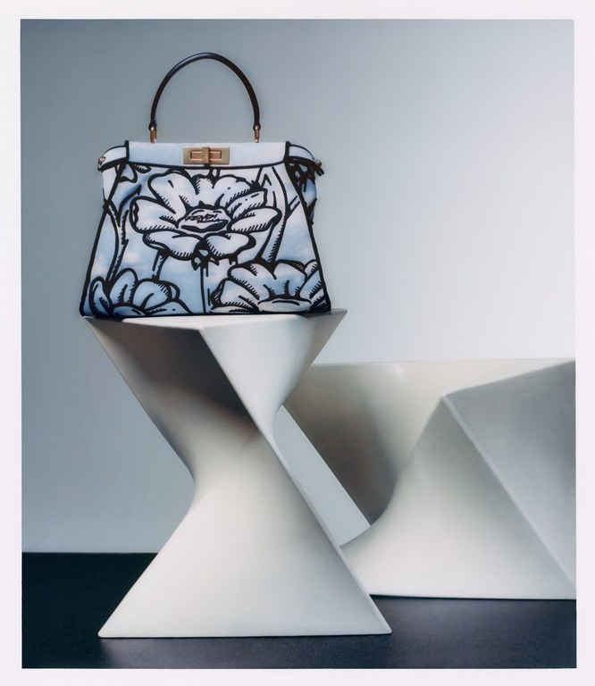 Luxury handbag with floral design displayed on a modern white stool in a studio setting. Fashion and design-focused product shot.