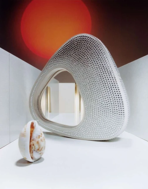 Contemporary shot featuring an abstract triangular mirror with a textured frame, paired with a decorative seashell in a minimalist setting.