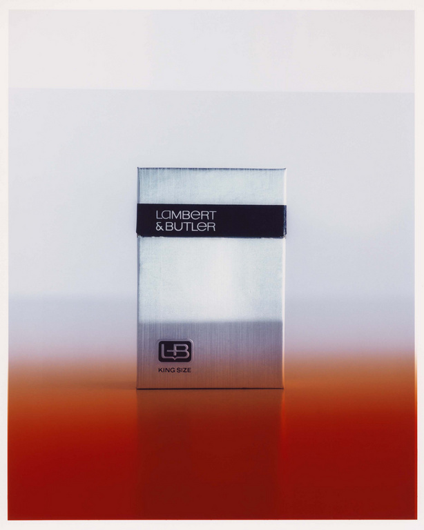 Close-up studio shot of a silver Lambert & Butler cigarette box, with a red gradient at the bottom, against a gradient white backdrop.