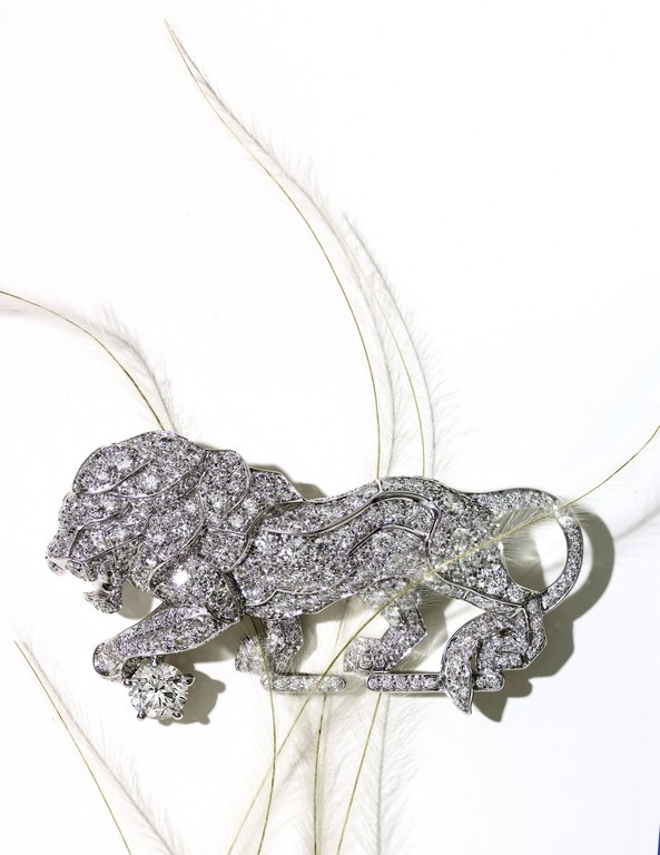 Close-up of a decorative silver brooch shaped like a lion encrusted with gems, set against a backdrop of delicate white feathers.