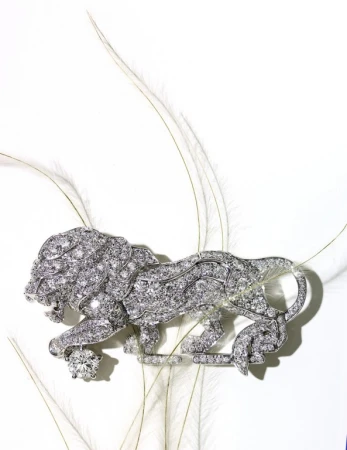 Close-up of a decorative silver brooch shaped like a lion encrusted with gems, set against a backdrop of delicate white feathers.
