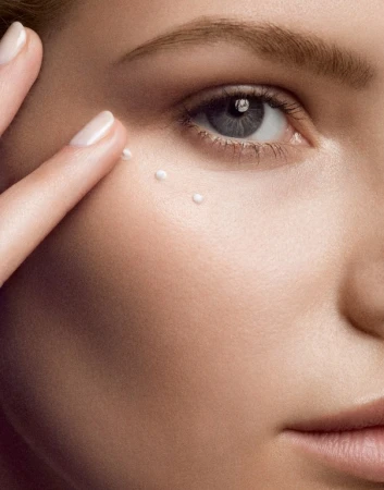 Close-up of a woman applying skincare cream under her eye with her finger, showcasing beauty and skincare in a neutral setting.