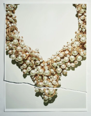 Close-up of a stylish pearl necklace, draped on a torn piece of paper against a white background in a studio lighting setup.
