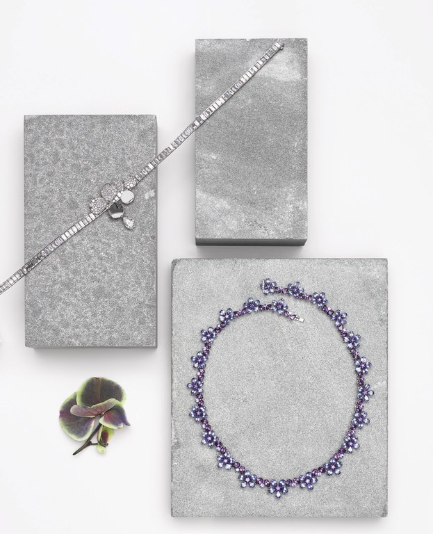 Elevated view of silver bracelets and necklace displayed on grey blocks with an orchid bloom on a white surface.
