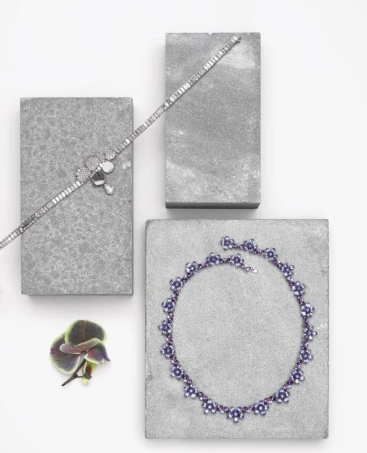 Elevated view of silver bracelets and necklace displayed on grey blocks with an orchid bloom on a white surface.