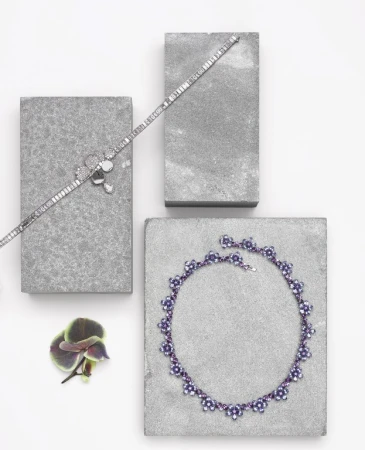 Elevated view of silver bracelets and necklace displayed on grey blocks with an orchid bloom on a white surface.