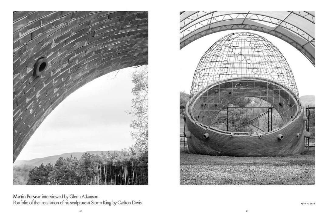 Black and white image featuring a close-up of a brick archway and a sculpture with an intricate metal frame in an outdoor setting.