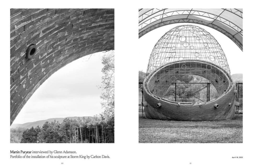 Black and white image featuring a close-up of a brick archway and a sculpture with an intricate metal frame in an outdoor setting.