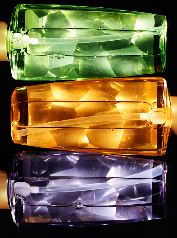 Still life of stacked translucent bottles in green, amber, and violet colors against a dark backdrop. Close-up abstract composition.