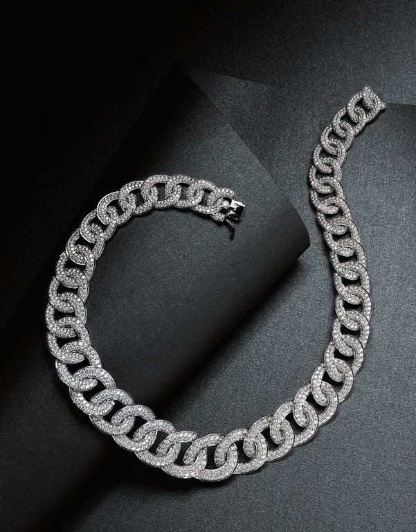 Close-up shot of a chunky silver chain necklace made of interlocking circles covered in gemstones on a black folded paper surface.