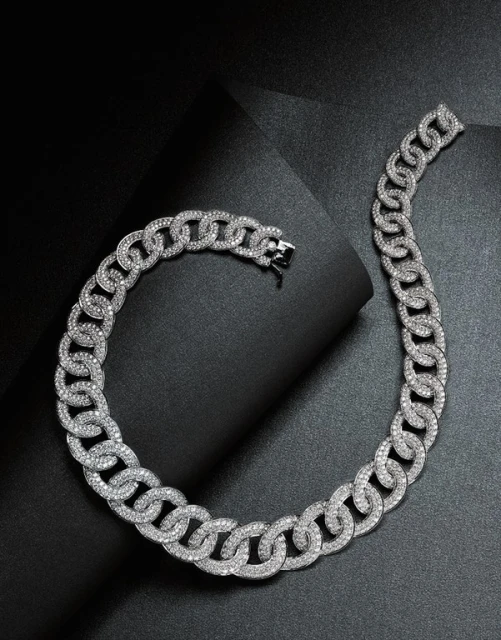 Close-up shot of a chunky silver chain necklace made of interlocking circles covered in gemstones on a black folded paper surface.