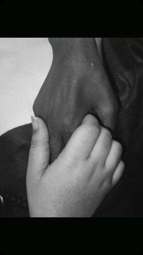 Monochrome image of two hands, one with darker skin holding the other with lighter skin, emphasizing connection and support.