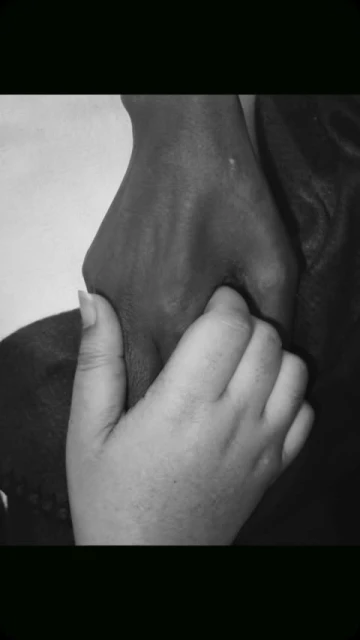 Monochrome image of two hands, one with darker skin holding the other with lighter skin, emphasizing connection and support.