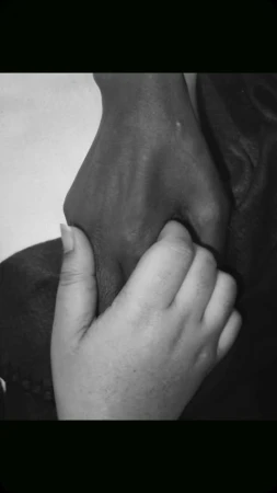 Monochrome image of two hands, one with darker skin holding the other with lighter skin, emphasizing connection and support.