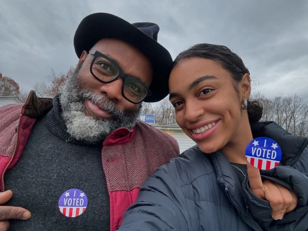 Smiling man and woman pose together outdoors, wearing 'I Voted' stickers, capturing a moment of civic engagement on a cloudy day.