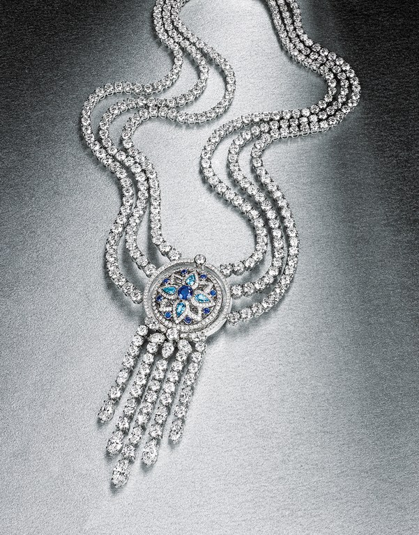 Elegant diamond necklace featuring cascading strands and a blue gemstone floral design on a metallic silver backdrop, jewelry photography.