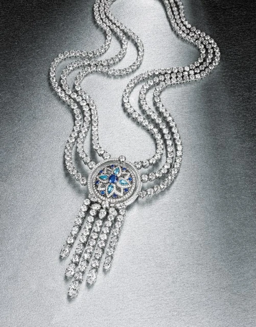 Elegant diamond necklace featuring cascading strands and a blue gemstone floral design on a metallic silver backdrop, jewelry photography.