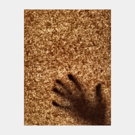 Shadow of a hand with fingers spread against a textured, mottled brown background, creating an eerie, abstract, and somewhat ominous effect.