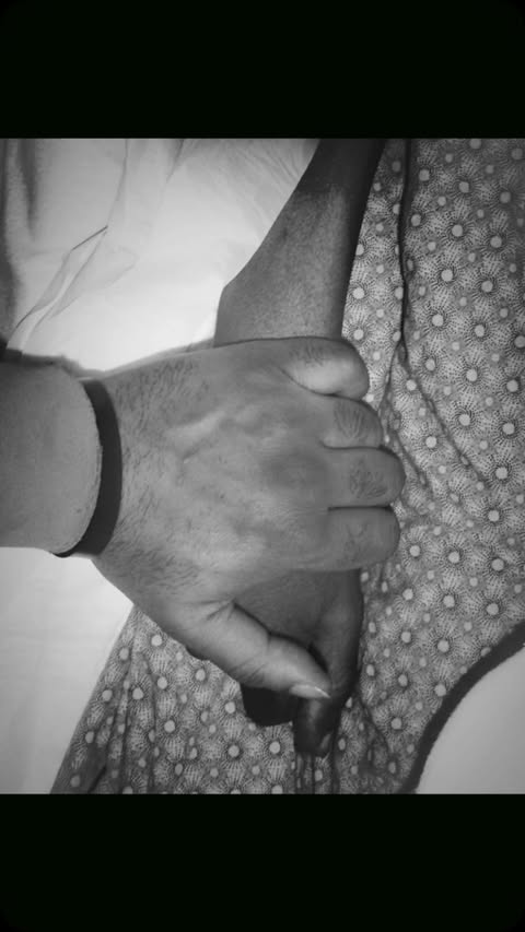 Monochrome image of a pair of hands clasped together, one with a dark wristband, against a background of patterned fabric.