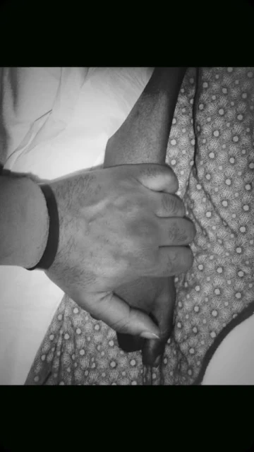 Monochrome image of a pair of hands clasped together, one with a dark wristband, against a background of patterned fabric.