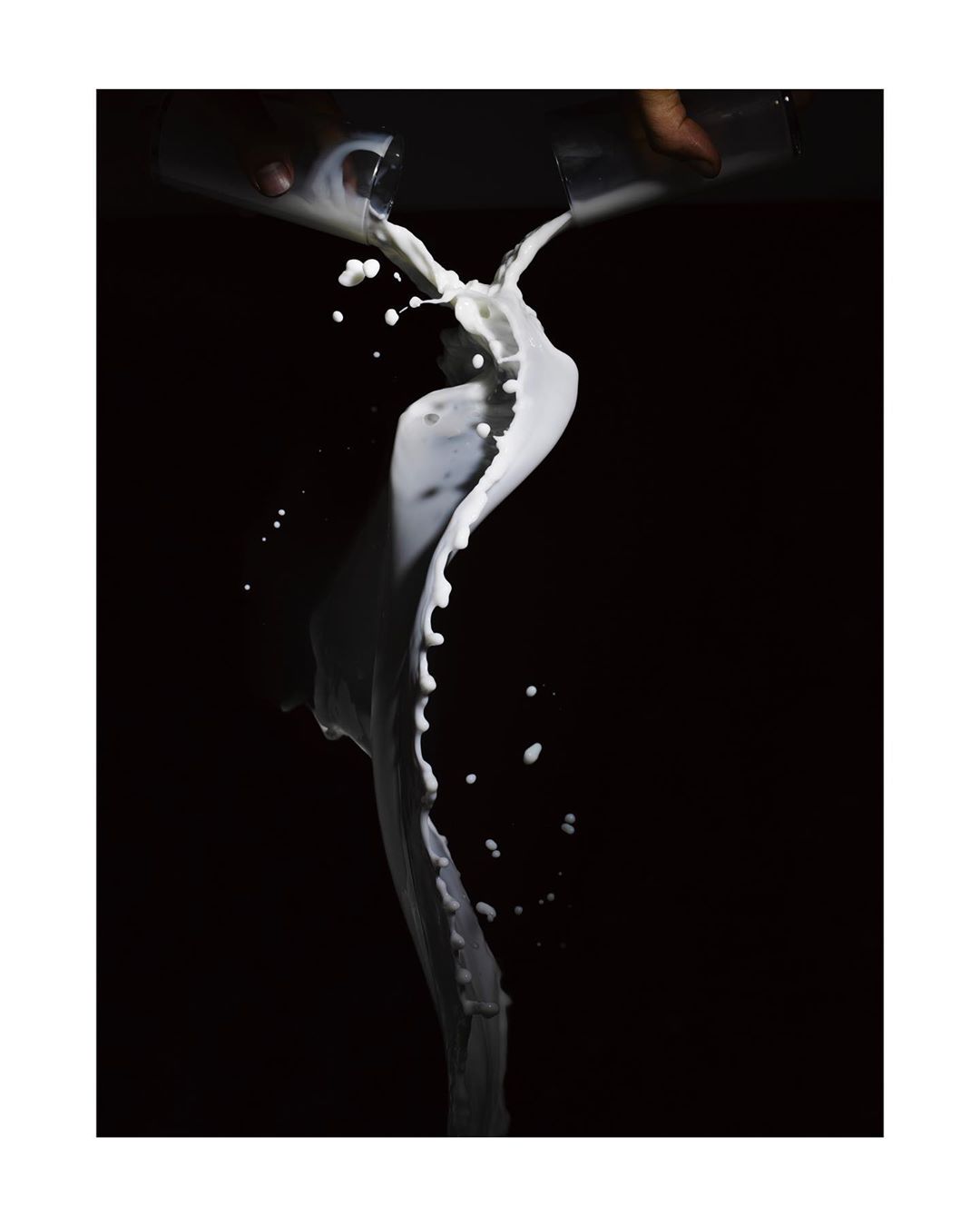 Dramatic studio shot of milk pouring from two glasses, showcasing a dynamic splash against a stark black backdrop.
