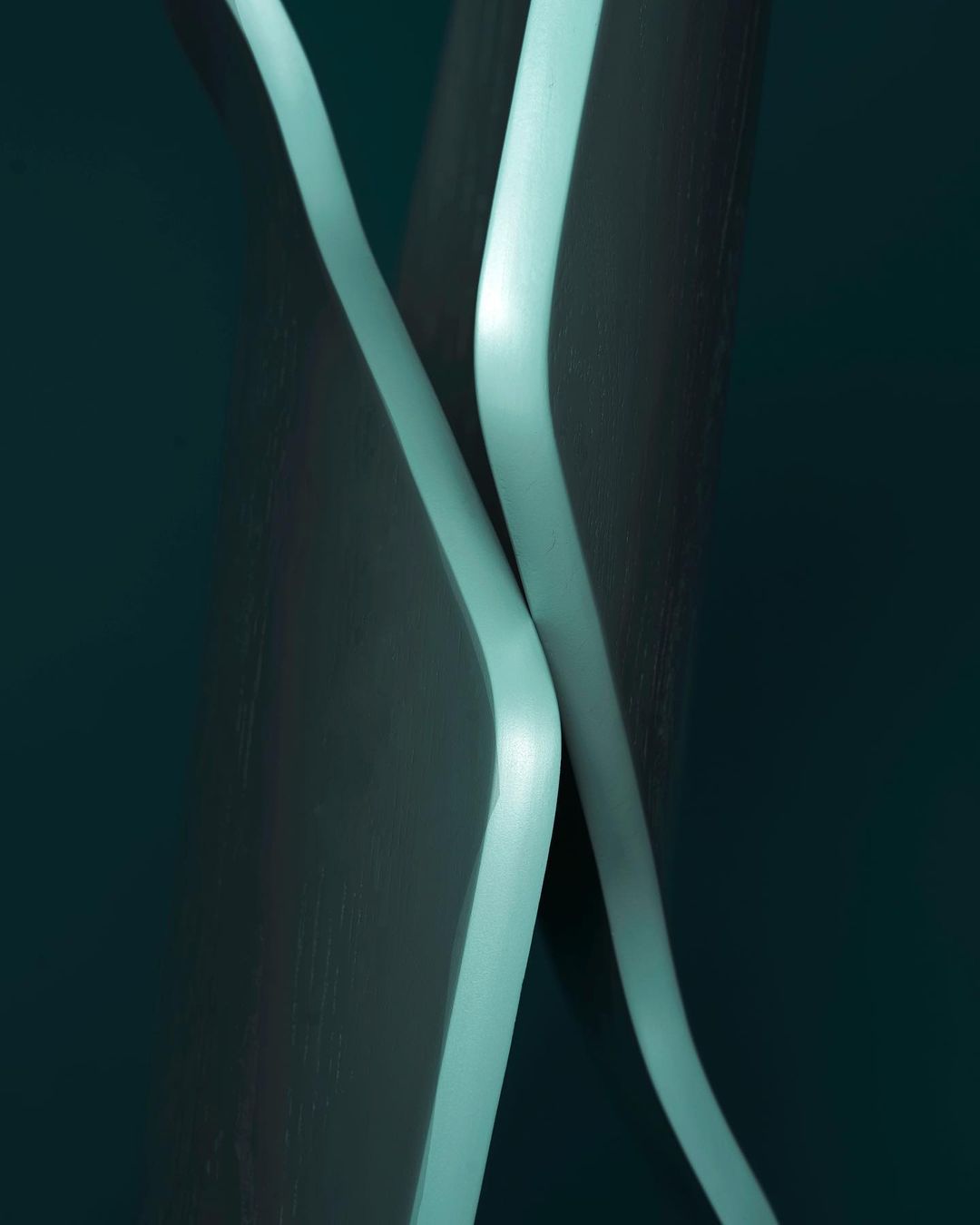 Abstract image of two curving forms with teal edges against a dark teal background, creating a minimalist yet visually striking composition.