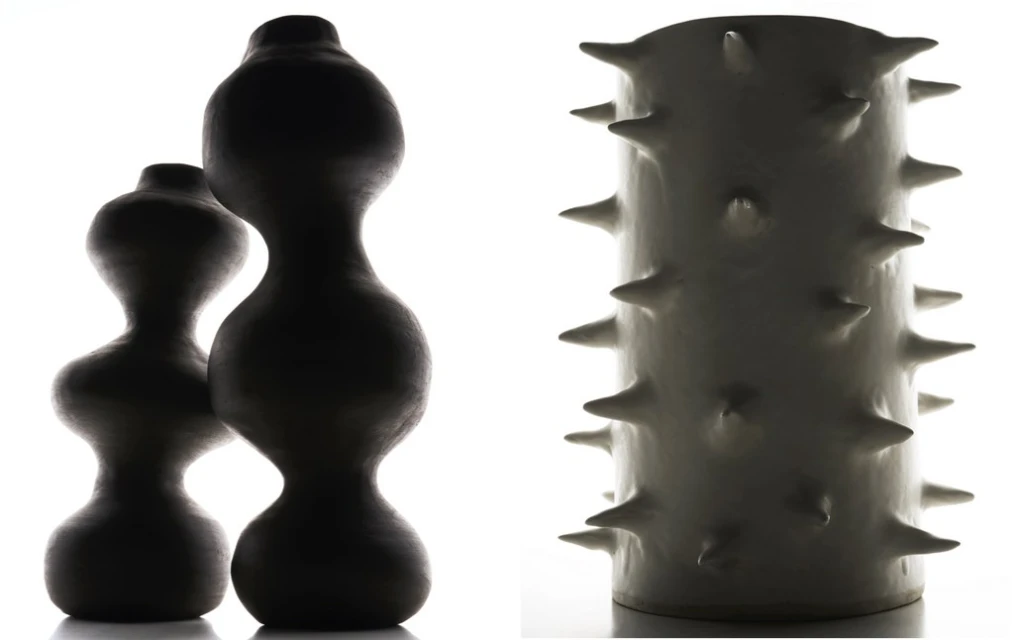 Two dark, smooth vases with curved silhouettes and a white vase with spike-like protrusions in a studio with a white backdrop.