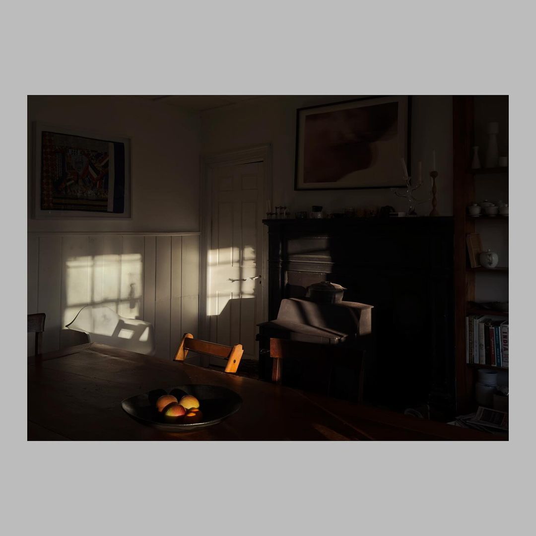 Warm, inviting scene of a wood table holding peaches in a bowl bathed in sunlight streaming through a window in an interior setting.