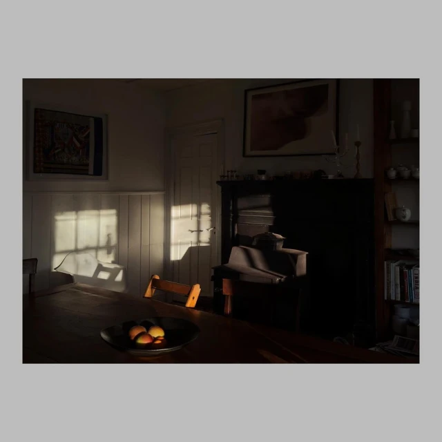 Warm, inviting scene of a wood table holding peaches in a bowl bathed in sunlight streaming through a window in an interior setting.