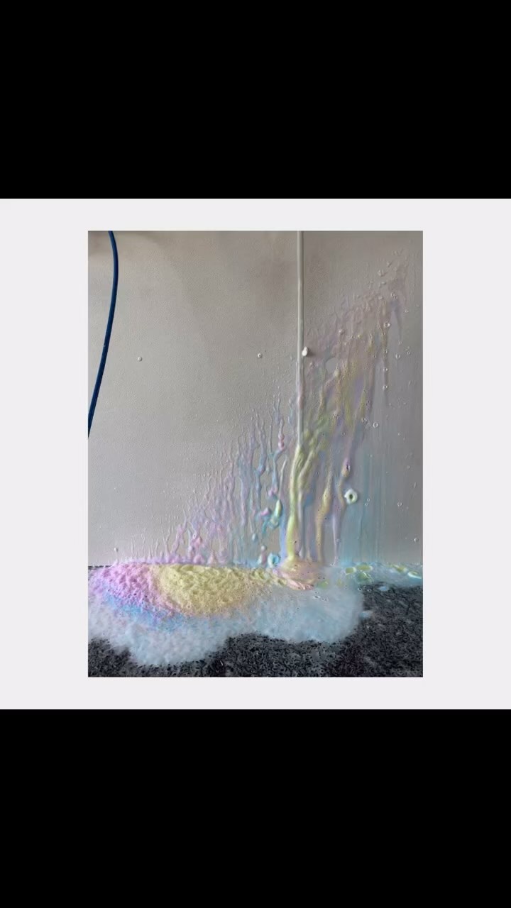 Abstract imagery of colorful water running down a white wall onto a dark grey floor with a white background and blue accent.