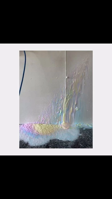 Abstract imagery of colorful water running down a white wall onto a dark grey floor with a white background and blue accent.